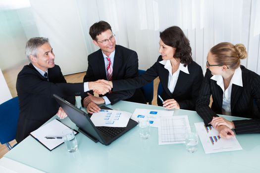 Busines colleagues seated around a table in a meeting congratulating one another by shaking hands