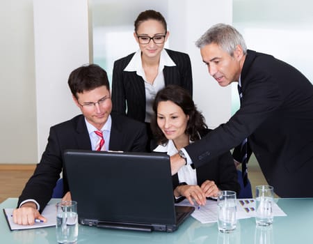 Four diverse professional businesspeople having a discussion and brainstorming session gathered around a laptop computer
