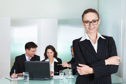 Corporate advancement and leadership concept with a confident smiling attractive businesswoman wearing glasses standing with her arms folded