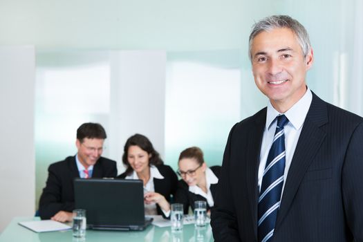 Corporate promotion and leadership concept with a successful handsome smiling businessman standing in the foreground while his colleagues