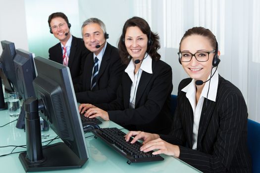 Line of professional stylish call centre operators wearing headsets seated behind their computers giving assistance