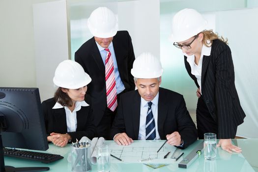 Meeting of four diverse architects or structural engineers in hardhats and suits seated in an office
