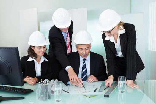 Meeting of four diverse architects or structural engineers in hardhats and suits seated in an office