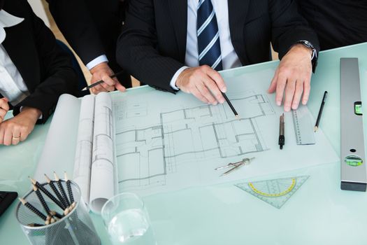 Cropped high angle view of the hands of a group of architects discussing a blueprint or architectural drawing laid out on a tabletop