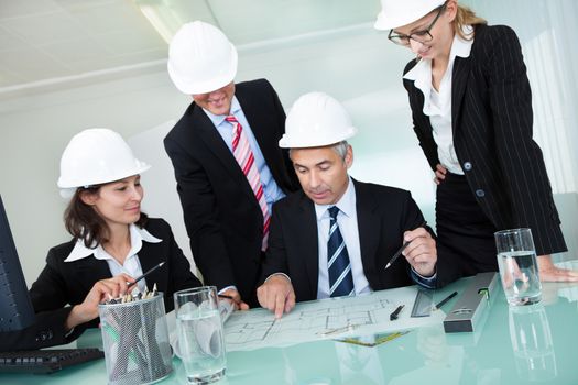 Meeting of four diverse architects or structural engineers in hardhats and suits seated in an office