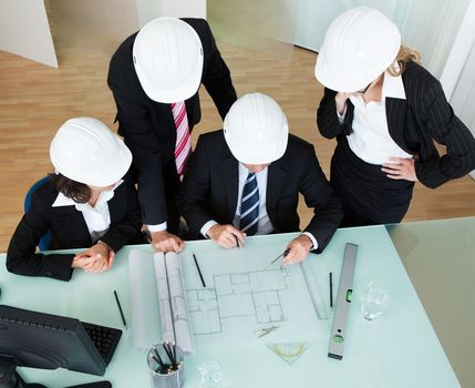 Overhead view of a group of architects or structural engineers discussing a blueprint laid out on the table in front of them