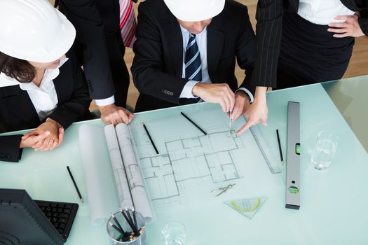 Overhead view of a group of architects or structural engineers discussing a blueprint laid out on the table in front of them