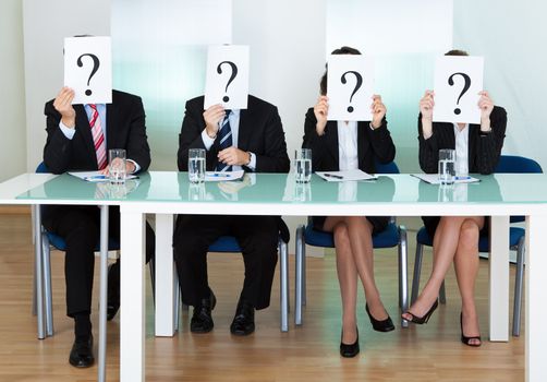 Row of businesspeople with question marks signs in front of their faces