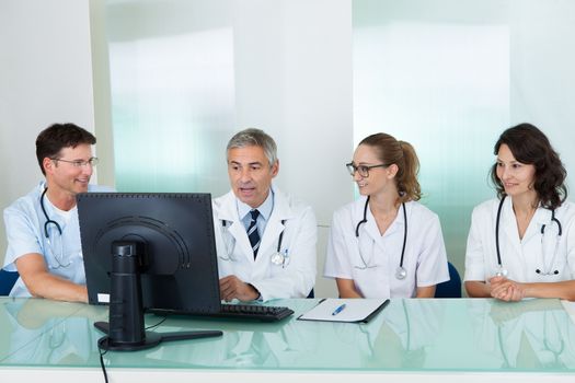 Doctors having a meeting seated at a table in front of a computer discussing case histories