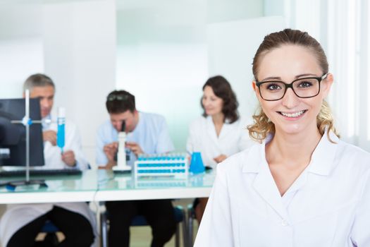 Attractive smiling female lab technician or technologist wearing glasses standing in the foreground