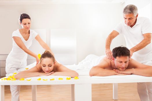 Professional masseurs in a spa giving back massages to an attractive husband and wife lying side by side