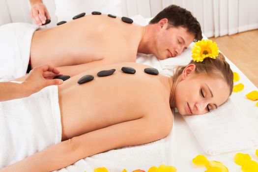 Couple having a hot stone massage treatment in a spa relaxing as the heat from the stones relaxes their muscles