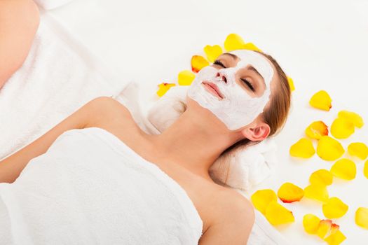 Therapist applying a face mask to the face of a beautiful young blonde woman using a cosmetic brush