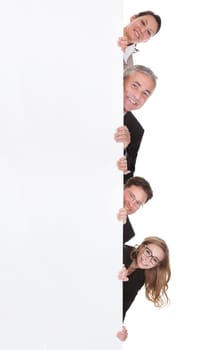 Four diverse professional businesspeople peering around the edge of a tall blank white banner with copyspace isolated on white