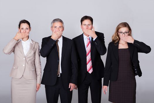 Four diverse businesspeople standing in a row gesturing for silence in a conceptual representation of the saying - Speak no evil