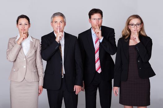 Four diverse businesspeople standing in a row gesturing for silence in a conceptual representation of the saying - Speak no evil