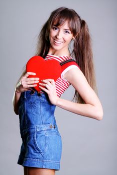 Portrait of a charming young girl on a white background holding a heart
