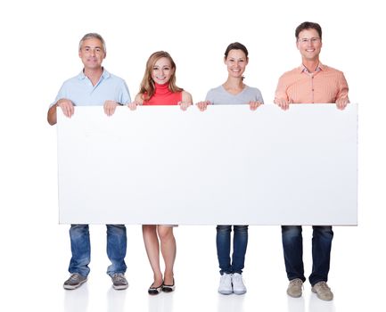 Two happy attractive middle-aged couples in casual clothing holding up a blank horizontal board or banner isolated on white