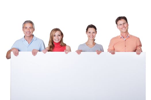 Two happy attractive middle-aged couples in casual clothing holding up a blank horizontal board or banner isolated on white