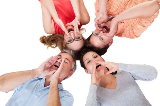 Conceptual image of four middle-aged friends calling out with their hands to their mouths and their heads together isolated on white