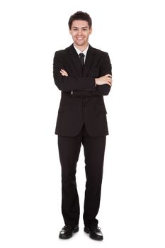 Full length studio portrait on white of a smiling confident young businessman standing with folded arms