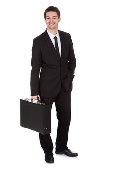 Full length studio portrait on white of a smiling confident young businessman standing with suitcase