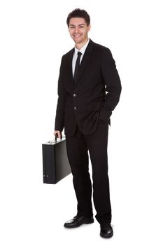 Full length studio portrait on white of a smiling confident young businessman standing with suitcase