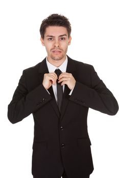 Half body portrait of a handsome young businessman standing straightening his tie isolated on white