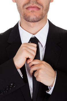 Half body portrait of a handsome young businessman standing straightening his tie isolated on white