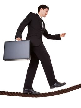 Conceptual image of a businessman carrying a briefcase balancing precariously as he walks a tightrope isolated on white