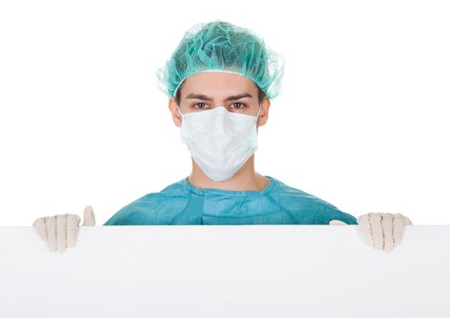 Young male surgeon in a cap and mask holding up a blank banner with copyspace for your text