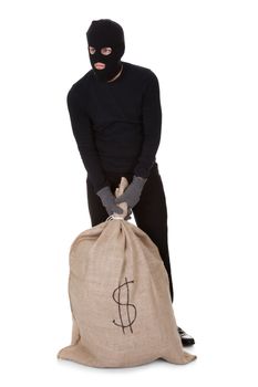 Thief in black clothes wearing a balaclava carrying a large bag of money with a dollar sign isolated on white