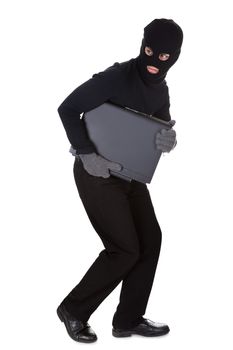 Thief dressed in black and wearing a balaclava stealing a laptop computer and making a furtive escape isolated on white