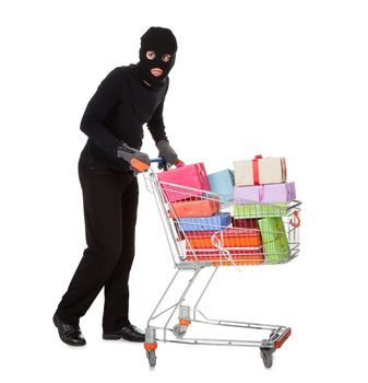 Thief in a black costume and balaclava pushing a shopping trolley full of gifts and presents from a celebration isolated on white