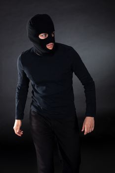 Thief wearing a balaclava dressed in blacked moving stealthily through the darkness as he prepares to commit robbery