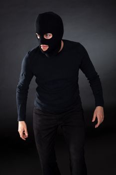 Thief wearing a balaclava dressed in blacked moving stealthily through the darkness as he prepares to commit robbery