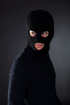 Thief wearing a balaclava dressed in blacked moving stealthily through the darkness as he prepares to commit robbery