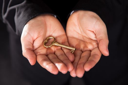 Conceptual closeup cropped image of an old-fashioned brass key held in outstretched cupped male hands