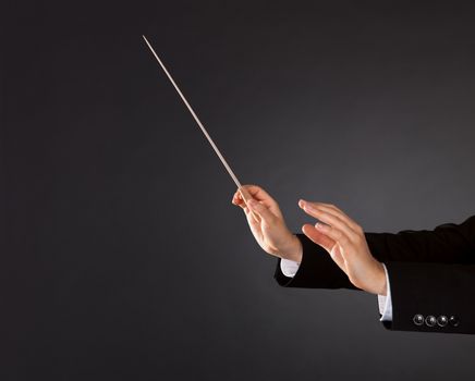 Closeup of the hands of a music conductor with a baton against a dark studio background with copyspace