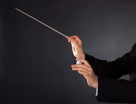 Closeup of the hands of a music conductor with a baton against a dark studio background with copyspace