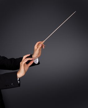 Closeup of the hands of a music conductor with a baton against a dark studio background with copyspace