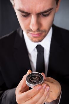 Businessman looking at a compass which he is holding in his hand with focus to the compass