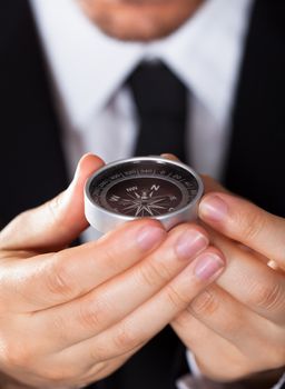 Businessman looking at a compass which he is holding in his hand with focus to the compass