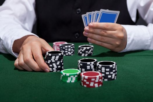 Male poker player about to place a bet moving a stack of tokens towards the centre of the gaming table with his free hand