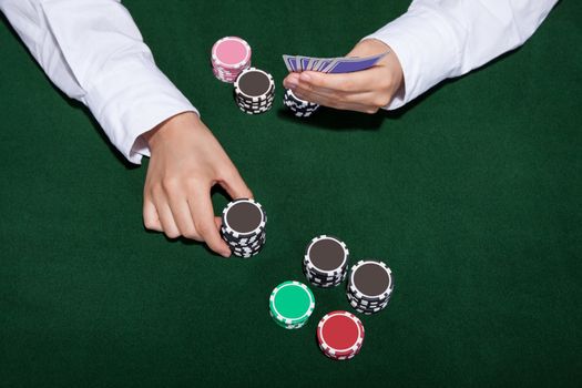 Male poker player about to place a bet moving a stack of tokens towards the centre of the gaming table with his free hand