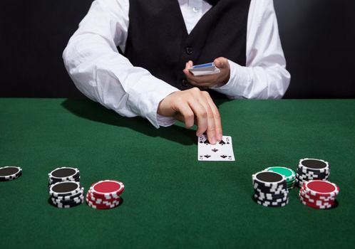 Croupier dealing cards in a poker game placing them face up on the green baize of the gaming table