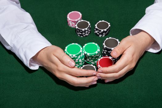 Croupier collecting in the bets at a casino table with his hands encircling various stacks of tokens or chips