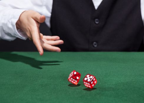 Croupier throwing a pair of red dice across the green felt on a card table in a casino in a game of chance