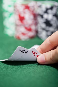 Hand of a male poker player lifting the corners of two cards on the green felt checking a pair of aces
