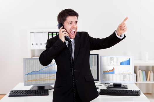 Enthusiastic young male stock broker in a bull market holding a telephone and yelling out a buy or sell order on stocks or bonds